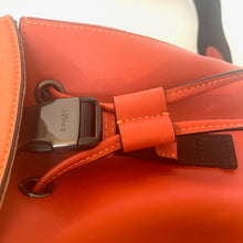 Load image into Gallery viewer, Close-up of an orange leather bag with a visible brand logo.