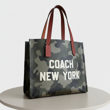 Load image into Gallery viewer, Camouflage-patterned handbag with 'Coach New York' text on a light gray background