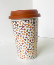 Load image into Gallery viewer, A white paper coffee cup with a brown lid, featuring an all-over interlocking geometric pattern in brown, tan, and orange. The brand name 'color' is printed near the bottom.