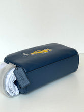 Load image into Gallery viewer, A navy blue leather zippered pouch with a gold embroidered logo, shown with a white fabric insert partially pulled from the side, on a plain white background.
