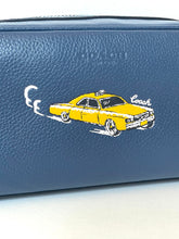 Load image into Gallery viewer, A close-up of a navy blue pebbled leather Coach pouch featuring an embroidered yellow cab illustration with the Coach logo.