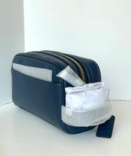 Load image into Gallery viewer, A navy blue leather zippered pouch or cosmetic case with a silver zipper, shown on a white surface against a white background. A white tissue or paper product is tucked into the side pocket, and a small dark tag is attached near the bottom right.
