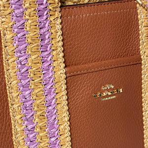 Close-up of a brown leather wallet with purple and gold woven strap, featuring the Coach logo.