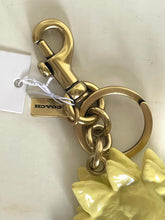 Load image into Gallery viewer, A Coach keychain featuring a polished gold-tone lobster clasp, split key rings, and a yellow faux-fur charm, shown with its white paper tag.