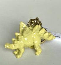 Load image into Gallery viewer, A small pale yellow dinosaur keychain figurine with a metallic gold ring and chain, photographed on a plain light background.
