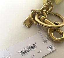 Load image into Gallery viewer, A gold-tone metal keychain or bag charm with a large lobster clasp and attached white retail tag, photographed on a plain light background.