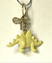 Load image into Gallery viewer, A pale yellow dinosaur keychain charm with a silver metal split ring, lobster clasp, and key ring, shown against a plain off-white background.