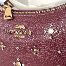 Load image into Gallery viewer, Close-up of a Coach handbag with decorative studs on a maroon background