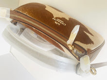 Load image into Gallery viewer, A Coach zippered pouch in brown and white cowhide with gold-tone hardware and a visible Coach logo, photographed on a white surface with white protective wrapping still attached.