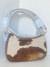 Load image into Gallery viewer, A Coach shoulder bag in brown and cream cowhide with a silver-tone metal logo on the front, featuring a light gray protective plastic wrap around the handle and tags still attached.