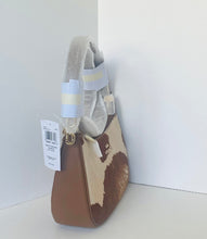 Load image into Gallery viewer, A small handbag with a brown and beige cow-print pattern, featuring a light gray plush handle wrapped in protective plastic and a white product tag attached.