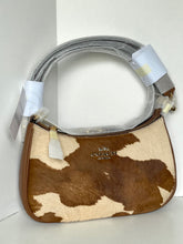 Load image into Gallery viewer, A Coach shoulder bag with a brown and beige cowhide pattern, featuring a gray strap wrapped in protective plastic and white hang tags.