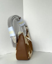 Load image into Gallery viewer, A brown and beige cowhide shoulder bag with a wide gray fabric strap, standing in the corner of a white room.