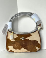 Load image into Gallery viewer, A Coach shoulder bag with a brown and beige cowhide pattern, featuring a gray fabric handle wrapped in protective paper and white product tags.