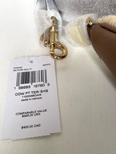 Load image into Gallery viewer, A close-up of a cow-print plush toy with a white and tan patch, a gold metal clasp, and a white price tag attached, photographed on a light surface.