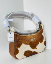 Load image into Gallery viewer, A Coach shoulder bag in brown and cream cowhide with a smooth brown leather base, featuring a protective plastic wrap on the handle and a hanging COACH tag.