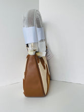 Load image into Gallery viewer, A small brown and cream cowhide shoulder bag with a light gray fabric strap, wrapped in protective plastic and tape at the top, standing in a white corner.