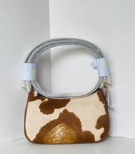 Load image into Gallery viewer, A small shoulder bag with a brown and cream cowhide pattern, featuring a gray faux-leather handle wrapped in protective plastic and secured with white tape. The bag is photographed in a minimalist white corner setting.