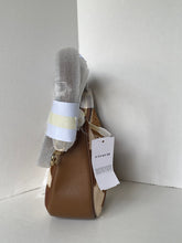 Load image into Gallery viewer, A Coach shoulder bag in brown leather, still wrapped in protective plastic and attached with a white brand tag, set against a plain white corner background.