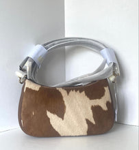Load image into Gallery viewer, A small shoulder bag with a brown and cream cowhide pattern, featuring a silver-toned metal handle wrapped in protective plastic and a white paper tag attached.