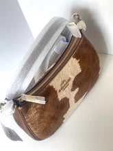 Load image into Gallery viewer, A brown and cream cowhide shoulder bag with a gold zipper, partially wrapped in protective white paper packaging, on a white background.