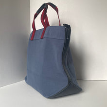 Load image into Gallery viewer, Blue tote bag with red handles on a light gray background