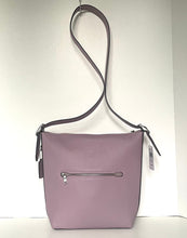 Load image into Gallery viewer, A light purple pebbled leather shoulder bag with a silver zipper front pocket and a dark brown shoulder strap, shown hanging against a white wall.