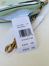 Load image into Gallery viewer, A Coach zip pouch in light pistachio green and white with gold hardware, shown with its original hangtag and clasp on a light surface.