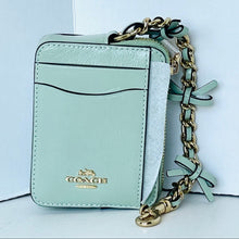 Load image into Gallery viewer, A Coach mini crossbody phone bag in light mint green leather, featuring a gold-tone chain strap, bow details, and a gold Coach logo on the front.