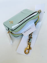 Load image into Gallery viewer, A Coach mini card holder in light sage green textured leather with gold hardware, shown with its white branded dust bag and hangtag on a white surface.