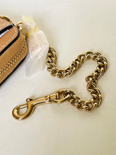 Load image into Gallery viewer, A close-up of a chunky gold-tone metal chain strap attached to a gold clasp, laid on a light beige surface next to part of a tan leather bag with a white protective paper.