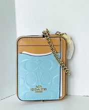 Load image into Gallery viewer, A Coach crossbody phone bag in light blue and tan leather with a gold chain strap, shown standing upright against a white background.
