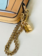 Load image into Gallery viewer, Close-up of a tan leather wallet or card holder with a gold-tone chain strap and padlock charm on a light neutral background.