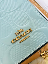 Load image into Gallery viewer, Close-up of a Coach New York wallet in light blue patent leather with the embossed signature C pattern and gold-tone metal logo hardware.