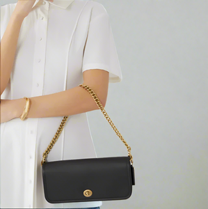 Black handbag with gold chain strap held by a person wearing a white shirt.