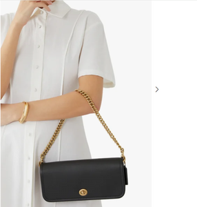 Black handbag with gold chain strap held by a person wearing a white shirt.