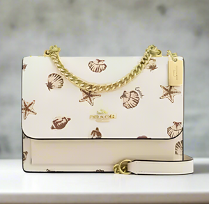 Designer handbag with shell pattern and gold chain on a white background