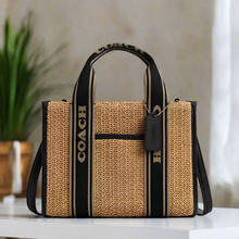 Load image into Gallery viewer, Coach handbag with straw-like texture and black accents on a white background