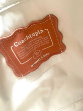 Load image into Gallery viewer, Close-up of a Coachtopia brand patch sewn onto a light beige fabric surface.