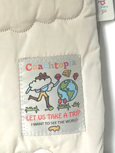 Load image into Gallery viewer, Close-up of a cream-colored quilted fabric item featuring a sewn-on patch with the brand name 'Coachtopia' and a colorful cartoon illustration of a traveler with a map and the text 'LET US TAKE A TRIP I WANT TO SEE THE WORLD'.