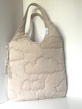 Load image into Gallery viewer, A quilted cloud-patterned shoulder bag in a light beige or cream color, standing against a plain white wall.
