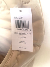 Load image into Gallery viewer, A close-up of a beige quilted garment with a white retail hangtag showing product details and pricing information.