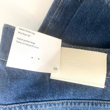 Load image into Gallery viewer, Close-up of blue jeans with a size tag and brand label.
