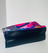 Load image into Gallery viewer, A zippered pouch with a glossy black front flap and a colorful abstract collage print in pink, blue, purple, and white on the body, shown on a plain white background.
