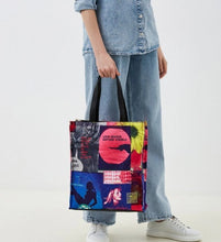 Load image into Gallery viewer, A person wearing a light blue denim shirt and wide-leg jeans holds a colorful tote bag with black handles. The tote bag features a collage print with red lips, a yellow flower, and text including 'LOVE MAKES SENSE NATURE VISIBLE'.