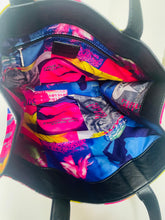 Load image into Gallery viewer, Open black tote bag showing a colorful printed interior lining with pink, blue, yellow, and gray graphic patterns and pockets.