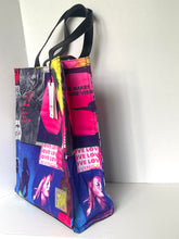 Load image into Gallery viewer, A tote bag with a vibrant collage print featuring pink, blue, black, and white panels with text and silhouettes, complete with black shoulder straps, photographed against a plain white background.