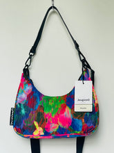 Load image into Gallery viewer, A colorful shoulder bag with a vibrant abstract floral pattern in pink, blue, green, and yellow, featuring black straps and a white Designdel tag.