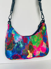 Load image into Gallery viewer, A small shoulder bag with a vibrant, multicolored abstract floral print featuring pink, blue, green, and red tones, with black plastic hardware and a black shoulder strap, shown against a plain white background.