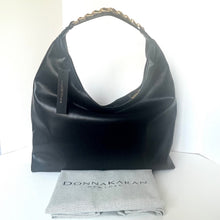 Load image into Gallery viewer, Black handbag with a gold chain detail on a white surface, accompanied by a branded cloth.